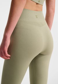 Olivgrön högmidjade leggings i texturerad tyg, med en slät midjeresår och subtila chevrondetaljer på baksidan.