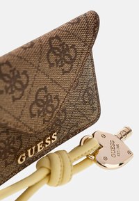 Bruine portemonnee met een patroon en een gestructureerde afwerking, gouden beslag en een hartvormig slot. Voorzien van gele leren accenten en een geperst logo.