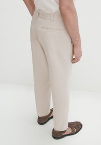 Beiga slim-fit byxor med platt midja och detaljer på bakfickan, i kombination med bruna sandaler. Slät textur och skräddarsydd form.