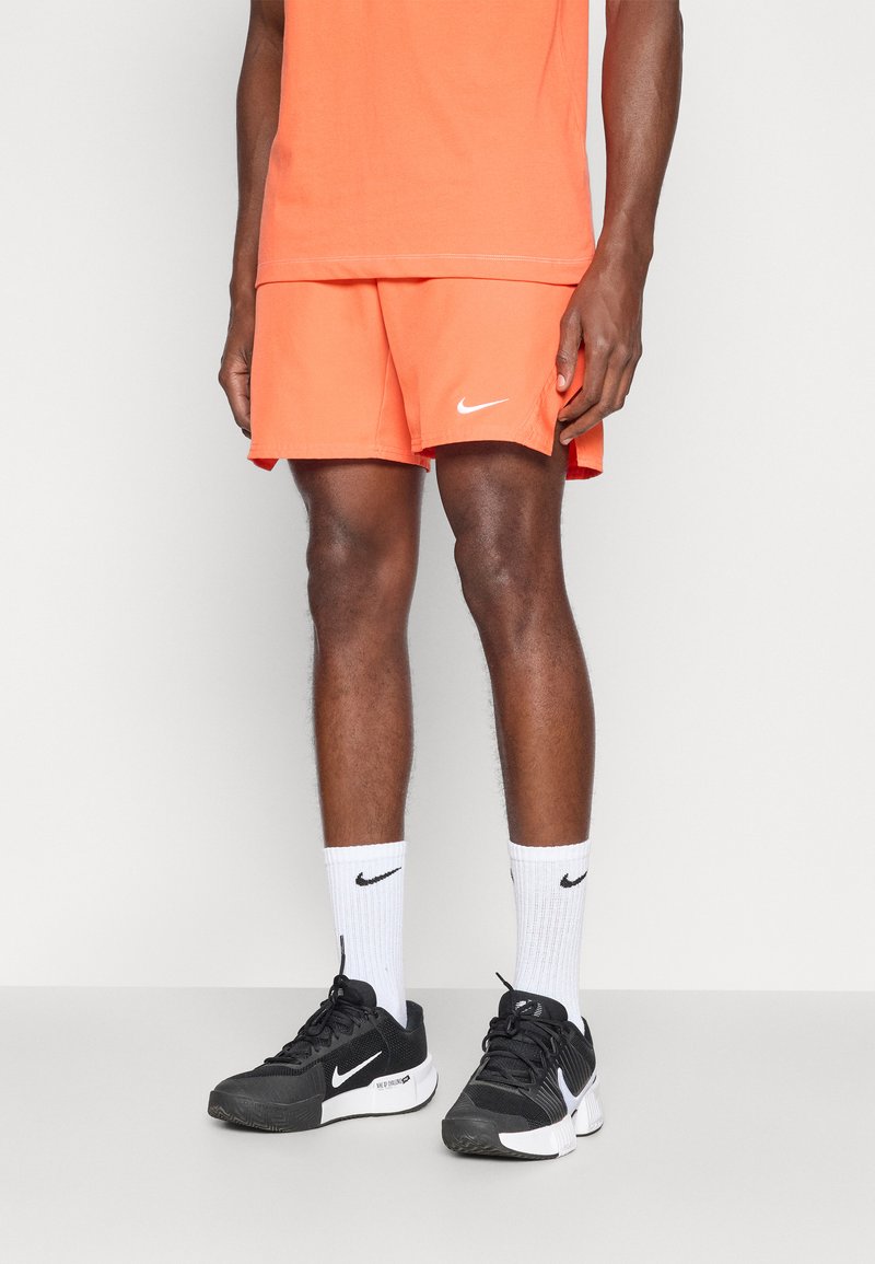 Πορτοκαλί σορτσάκια Nike συνδυασμένα με μαύρα αθλητικά παπούτσια Nike και λευκές κάλτσες κατά του γόνατος. Τα σορτσάκια διαθέτουν το λευκό λογότυπο της Nike και έχουν άνετη γραμμή.