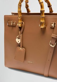 Borsa in faux leather marrone con manici in bambù, dettagli in hardware dorato e un'etichetta a forma di cuore. Include una tracolla staccabile.