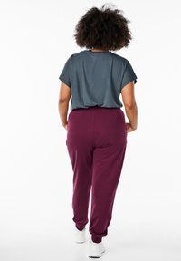 Graues Kurzarmoberteil kombiniert mit burgunderroten Sweatpants, die elastische Bündchen an den Knöcheln und eine lockere Passform aufweisen. Weiße Schuhe runden das Outfit ab.