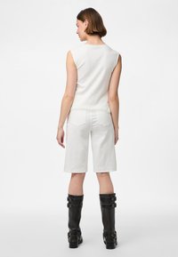 Witte geribbelde mouwloze top gecombineerd met witte shorts tot de knie en zwarte kniehoge laarzen met zilveren gespen. Achteraanzicht.