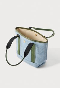 Μικρή τσάντα χειρός ανοιχτού γαλάζιου χρώματος με πράσινο περίγραμμα και μαύρες λαβές, ανοιχτή κορυφή με χρυσό κουμπί κλεισίματος, μπεζ εσωτερικό, τοποθετημένη σε λευκό φόντο.