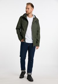 Vandafvisende grøn jakke med hætte, lynlås og knaplukninger, samt to frontlommer, parret med mørke jeans og sorte støvler.