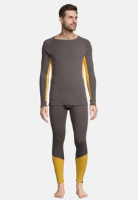 Langærmet termotop og leggings i grå med gule accenter, der har en figursyet design og blød tekstur, velegnet til lagdeling.
