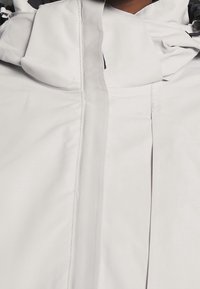 Gros plan sur une veste gris clair avec un col montant et une fermeture éclair avant dissimulée.