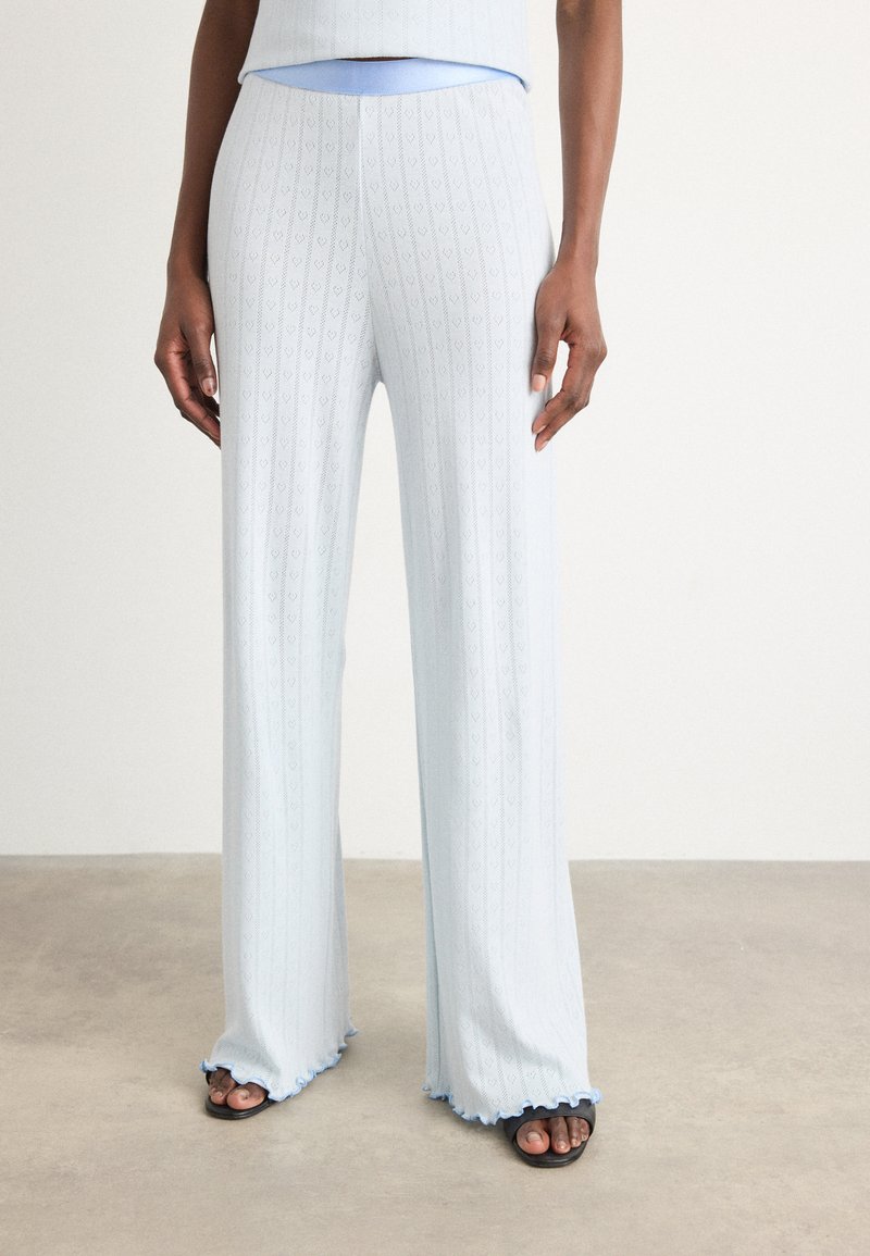 Himmelblaue Strickhose mit einem strukturierten Herzmuster, ausgestellter Silhouette und Rüschensaum, kombiniert mit schlichten schwarzen Sandalen.