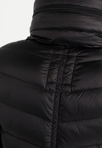 Mustapuffatakki, jossa on korkea kaulus, tikattu kuvio ja näkyvä vetoketju kaulan kohdalla, valmistettu sileästä, kiiltävästä materiaalista.