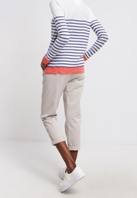 Pasiasty top z długim rękawem w białym i granatowym kolorze z koralowymi akcentami, zestawiony z beżowymi spodniami 3/4 i białymi trampkami. Gładkie faktury we wszystkich elementach.