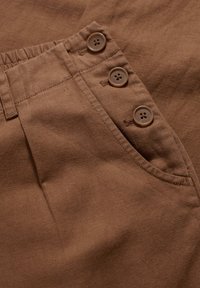 Brunt linnetyg med synlig textur, med en sidficka och tre bruna knappar längs midjan. Klassisk design med naturliga färger.