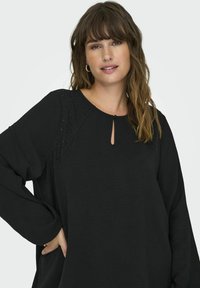 Černý dlouhý rukáv top s výstřihem do kulata, detaily ve tvaru klíče a ozdobnými rameny s malými hroty pro texturu a designový zájem.