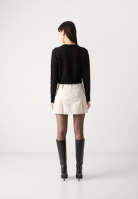 Svart stickad tröja med ribbat detalj, parat med en ljusbeige minikjol och knähöga svarta stilettklackar. Enfärgad genomgående.