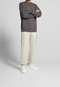 Grå sweatshirt med rund hals, kombinerad med krämfärgade cargobyxor med sidofickor. Vita sneakers complete outfiten.