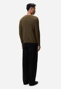 Olivgrön stickad tröja med ett strukturerat mönster, rund halsringning och långa ärmar, kombinerad med löst sittande svarta byxor.