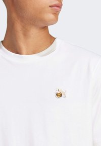 Hvid bomulds t-shirt med et broderet design af en hund og en basketball på brystet, med rund halsudskæring og korte ærmer.