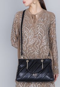 Svart vadderad läderhandväska med guldfärgade detaljer, med en kedjeaccent och logotyp. Väskan har en rektangulär form och justerbar rem.