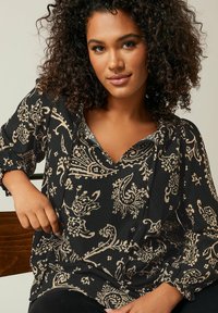 Blusa nera a fantasia realizzata in tessuto testurizzato, con swirls floreali beige, scollatura a V e maniche lunghe con polsini arricciati.