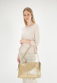 Złota skórzana torebka z wzorem w panterę, z długim paskiem, eleganckim designem i błyszczącą teksturą.