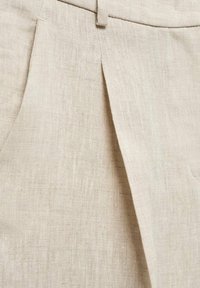 Un pantalon en lin beige avec une finition texturée, doté de plis à l'avant et d'une taille épurée.