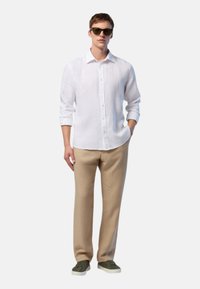 Camicia bianca a maniche lunghe con bottoni, dalla vestibilità ampia, abbinata a pantaloni beige e sneakers verdi. Tessuto liscio, dettagli di design minimi.