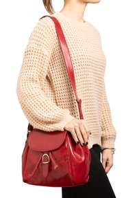 Borsa a tracolla in pelle rossa con design strutturato e pattina frontale. Caratterizzata da una tracolla regolabile e un dettaglio decorativo a fibbia.