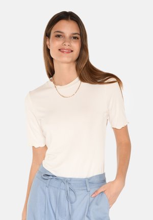 Krémový top s krátkým rukávem a vroubkovaným výstřihem, spárovaný se světle modrými kalhotami s vysokým pasem, které mají detail zavázaného pasu.