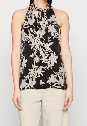 Czarny top na ramiączkach typu halter z beżowym kwiatowym wzorem i wiązaniem przy szyi, noszony z jasnobeżowymi spodniami.