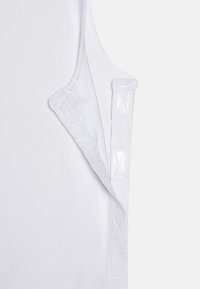 Haut sans manches blanc en coton lisse, avec un col côtelé et des bretelles texturées contrastantes arborant un motif de points en croix.