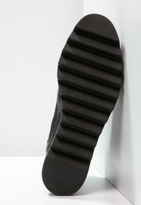 Kenkäpohja, jossa on leveät, vaakasuorat urat, nojaamassa valkoista kulma seinää ja lattiaa vasten, näyttäen pinnan kuvioita ja tekstuuria.