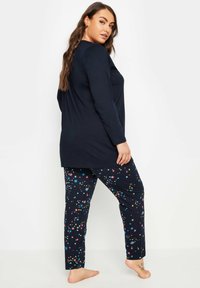 Marinblå långärmad tröja som matchas med marinblå byxor med ett färgglatt stjärnmönster. Materialet verkar mjukt med en avslappnad passform.