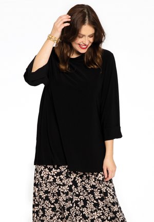 Schwarzes Langarmshirt mit rundem Halsausschnitt und umgeschlagenen Bündchen, kombiniert mit einem Blumenrock in Schwarz und Creme, glatte Stoffoberfläche.