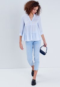 Blouse peplum rayée bleu clair avec un front à boutons et des manches trois-quarts, associée à un jean bleu clair et un petit sac noir.