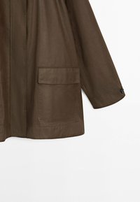 Brun frakkeærme og underkrop med stor forlomme med klap og manchet med knap på hvid baggrund.