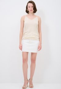 Beige v-hals camisole lavet af blødt stof, parret med en hvid denim miniskørt med rå kant og frontlomme, båret med beige hæle.