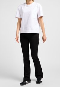 Vit t-shirt med kort ärm och ficka, i kombination med svarta utsvängda byxor och svarta sneakers med vita ränder. Slät bomullstextur.