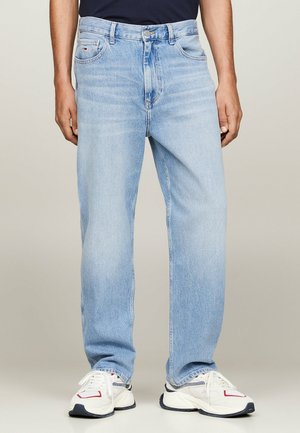 Jean bleu clair avec une coupe droite, dotés de cinq poches, d'une fermeture éclair et d'un léger délavage. Portés avec des baskets blanches.