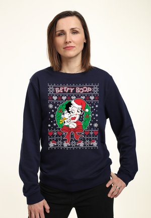 Navyblå sweatshirt med et Betty Boop grafik omgivet af festlige mønstre, herunder kristtorn, hjerter og snefnug i rød og hvid.