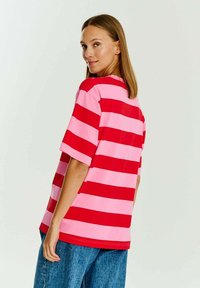 Červeno-růžové pruhované tričko s krátkým rukávem v volném střihu, vyrobené z měkkého materiálu. Má kulatý výstřih a boční rozparky pro snadný pohyb.