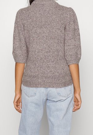Kvinde iført en grå strikket kortærmet sweater med pufærmer og lyseblå højtaljede jeans, set bagfra.