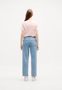 Chemise à manches courtes rose clair associée à un jean en denim bleu clair taille haute, présentant une coupe décontractée et des coutures discrètes sur les poches arrière.