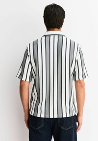 Short-sleeve shirt with vertical black and white stripes, a pointed collar, and a relaxed fit. Fabric has a subtle texture.
