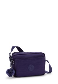 Pequeño bolso de hombro de color púrpura oscuro con un bolsillo frontal, correa ajustable y un llavero de mono esponjoso adjunto al tirador de la cremallera.