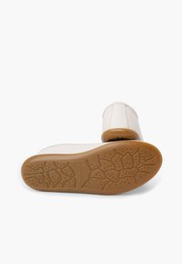 Botines blancos con suelas de goma color canela que muestran un patrón de dibujo texturizado, una bota en posición vertical y otra de lado sobre un fondo blanco.