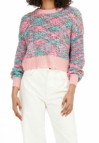 Pulls multicolores avec un motif tricoté texturé, dotés de poignets et d'un ourlet côtelés roses. Le look est complété par un pantalon blanc taille haute.