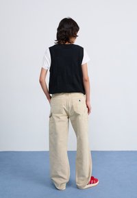 Svart stickad väst över en vit t-shirt, tillsammans med beige cargobyxor med sidofickor och en logotyp patch. Röda sneakers fulländar looken.
