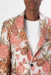 Blumiges Sakko mit einem gewebten Design in Pink, Orange und Grün auf einem hellen cremefarbenen Hintergrund; Ein-Knopf-Verschluss und strukturierter Kragen.