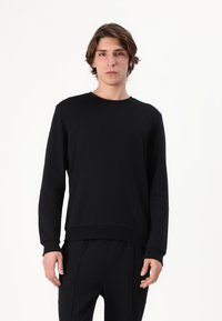 Melns crewneck džemperis no mīksta, teksturēta auduma ar garām piedurknēm un brīvu piegriezumu, ar ribotiem piedurkņu galiem un apakšmalu.