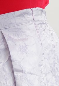 Primo piano di una gonna floreale jacquard lilla pallido con cerniera laterale, indossata con un top rosso brillante.