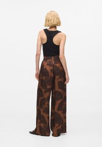 Široké nohavice v hnedej farbe s čiernym listovým vzorom, skombinované s čiernym tielkom. Nohavice majú vysoký pás a prúdenie látky.